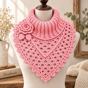 May include: A light pink crochet cowl neck scarf featuring a ribbed collar and a triangular lace pattern body. A three-dimensional crocheted rose with two leaves is attached to the upper left side of the scarf, which has a scalloped edge.