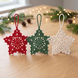 Può includere: Tre ornamenti a forma di stella realizzati in filo all'uncinetto nei colori rosso, verde scuro e bianco sporco. Ogni stella presenta un intricato motivo in pizzo traforato e un cappio in filo ritorto abbinato sulla parte superiore.