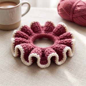 May include: A circular crochet hair scrunchie featuring a deep burgundy red center with a ruffled, wavy edge trimmed in a contrasting cream white yarn. The accessory has a textured, hand-stitched appearance with a gathered, elasticized design.