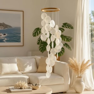 May include: A hanging mobile featuring a circular wooden frame with numerous translucent, off-white, circular discs suspended by thin strings. The discs are arranged in a cascading, layered formation, creating a delicate, light-reflecting structure that hangs vertically from the ceiling.