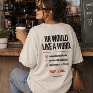 May include: An off-white short-sleeve t-shirt featuring black and red text on the back that reads: HR WOULD LIKE A WORD. Below this are three checkboxes marked with X's next to inappropriate behavior, questionable decisions, and unnecessary confidence.