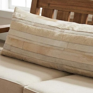 May include: A long rectangular lumbar pillow featuring a horizontal patchwork design of various textured strips in shades of cream, beige, and light tan. The pillow is positioned on a wooden bench with light-colored seat cushions.