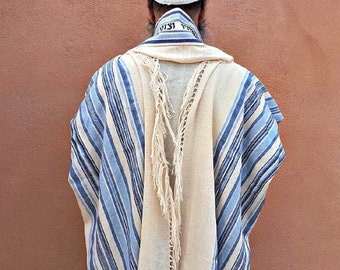 May include: A white prayer shawl with blue stripes and fringes. The shawl has Hebrew writing on the collar.