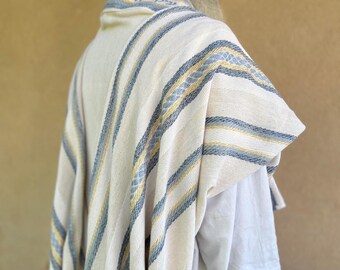 May include: A white prayer shawl with blue and yellow stripes. The shawl has Hebrew writing on the collar.