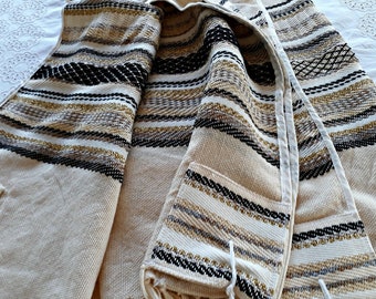 May include: A beige prayer shawl with black, gold, and silver stripes. The shawl is folded in half and has a fringe on the bottom.