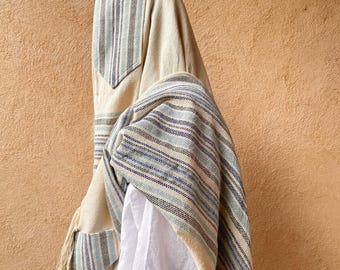 Puede incluir: Una chal de oración a rayas blancas y azules con flecos. La chal está doblada y drapeada sobre los hombros de una persona.