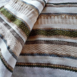 May include: A white prayer shawl with blue, green, and gold stripes. The shawl is folded in half, showing the intricate woven pattern.