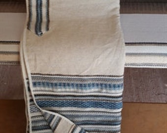May include: A white prayer shawl with blue and brown stripes. The shawl is folded in half and has a fringe on the bottom.
