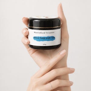 May include: A black cylindrical jar containing 150g of product. The white label features the text Moorishland Treasures and Black Soap with Nila in blue script. The jar has a black screw-top lid and a smooth, glossy finish on the container surface.