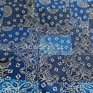 Puede incluir: Una tela de patchwork con un patrón de bandana de cachemira azul y blanco repetitivo. El tejido se compone de varios segmentos cuadrados en diferentes tonos de azul, incluyendo azul marino y azul claro, con el texto Indircraft visible.