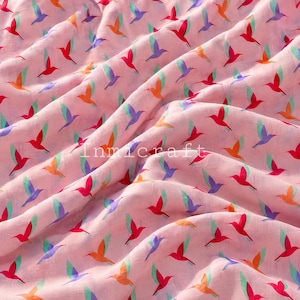 May include: A light pink fabric featuring a repeating pattern of small flying hummingbirds in shades of red, orange, purple, and teal. The textile has a soft, draped texture with the word Inmicraft printed in white across the centre.