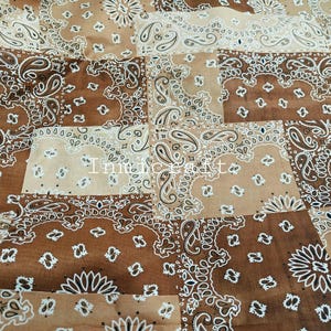 May include: A fabric featuring a patchwork design of brown and tan bandana patterns with white paisley and floral motifs. The word Innicraft is printed in white across the center of the textile, which displays a repeating geometric layout.