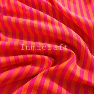 May include: A fabric featuring a repeating pattern of vibrant orange and bright pink diagonal stripes. The textile is draped in soft folds, creating a textured appearance. The word Inmicraft is printed in white text across the centre of the image.