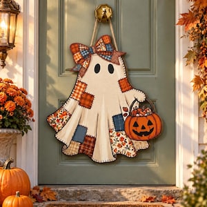 May include: A hanging ghost decoration featuring a cream-coloured body with various patchwork fabric patterns in orange, blue, and brown. The ghost has a large bow at the top and holds a bright orange jack-o'-lantern bucket filled with sweets.