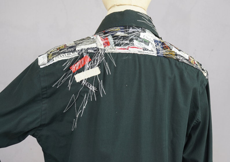May include: A dark green long-sleeved shirt with a patchwork design on the back. The design features various colorful fabric scraps and white stitching.