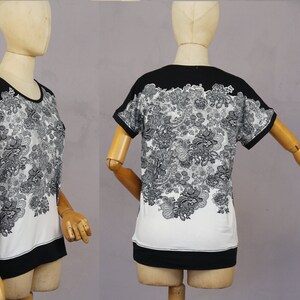 May include: A white and black short-sleeved shirt with a floral print. The shirt has a black band around the neck and a black band at the bottom.
