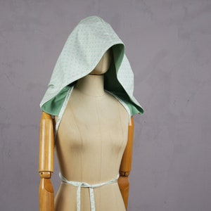May include: A light green hooded garment with a white polka dot pattern. The garment is tied at the waist with a matching fabric tie.