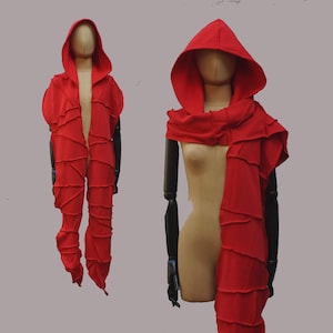 Könnte beinhalten: Ein leuchtend rotes Kapuzen- und Schal-Set. Das Outfit zeichnet sich durch ein einzigartiges Design mit geschichtetem, gerüschtem Stoff und Ziernähten aus. Die Kapuze ist übergroß, und der Schal fällt elegant. Das Set wird auf einer Schaufensterpuppe präsentiert.