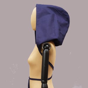 Könnte beinhalten: Eine marineblaue Kapuze mit passendem Bindeband. Die Kapuze ist aus einem weichen Stoff gefertigt und wird auf einer Schaufensterpuppe präsentiert. Die Kapuze ist als Kopfbedeckung konzipiert.