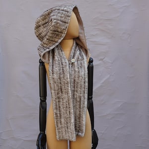 Könnte beinhalten: Ein gestreifter Kapuzen-Schal in Braun und Weiß mit einem Knopfverschluss. Der Schal ist aus einem weichen, flauschigen Material gefertigt und perfekt, um sich im Winter warm zu halten.