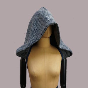 May include: A blue and white speckled hood with a quilted lining and a blue trim. The hood is displayed on a mannequin. The hood is designed to be worn over the shoulders.