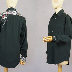 May include: A dark green long-sleeved button-up shirt with a unique design on the back and cuffs. The design features a variety of colorful fabrics and textures.