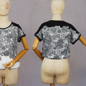 May include: Black and white short-sleeved shirt with a floral print. The shirt has a black collar and black trim on the sleeves.