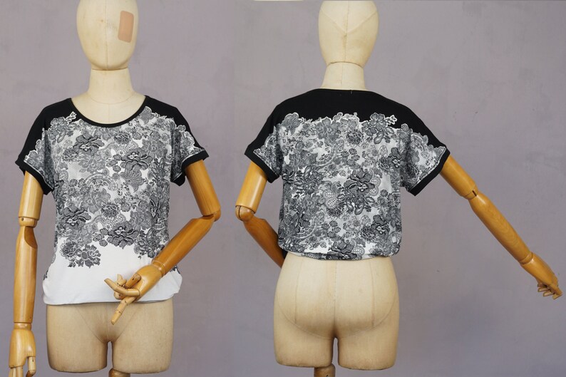 May include: Black and white short-sleeved shirt with a floral print. The shirt has a black collar and black trim on the sleeves.