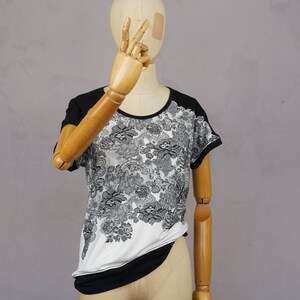 May include: A white and black floral print t-shirt with a black trim around the neckline and sleeves. The shirt is on a mannequin.