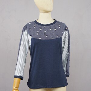 May include: A navy blue long-sleeved shirt with a white and blue striped pattern on the sleeves. The shirt has a distressed look with holes in the fabric. The shirt is made of a soft, comfortable material.