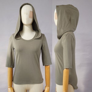 Può includere: Una maglietta a maniche lunghe con cappuccio di colore verde oliva. La maglietta ha una vestibilità comoda e un collo rotondo. Il cappuccio è attaccato alla maglietta e può essere indossato su o giù.