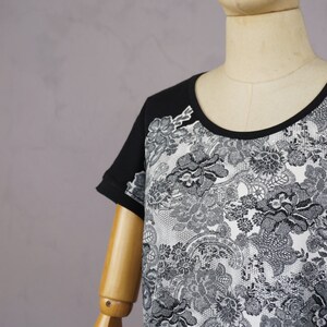 May include: Black and white short-sleeved shirt with a lace pattern. The shirt has a round neckline and is made of a soft, comfortable fabric.
