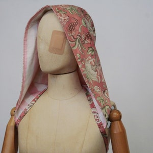 Könnte beinhalten: Ein rosa-weißer Kapuzen-Schal mit Blumenmuster. Der Schal ist aus Baumwollstoff und hat innen ein kariertes Muster.