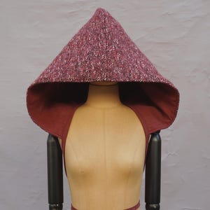 May include: A burgundy hooded cloak with a speckled pattern. The hood is lined with a solid burgundy fabric.