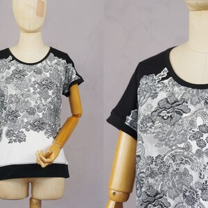 May include: A black and white short-sleeved shirt with a floral pattern. The shirt has a black collar and a white background with black floral designs.