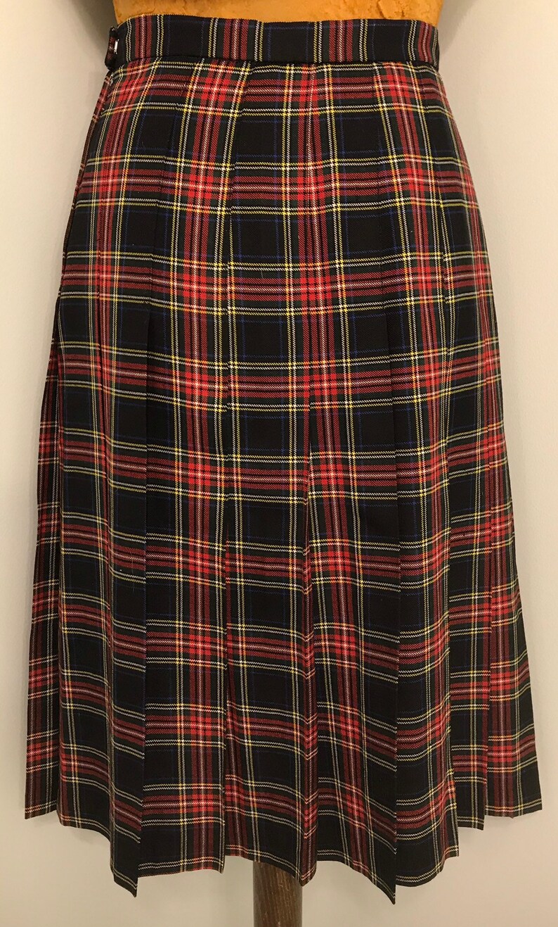 May include: A black, red, yellow, and white plaid pleated skirt. The skirt has a waistband with a button closure and is displayed on a mannequin. The fabric appears to be a medium-weight material. The skirt is a classic design.