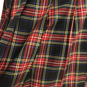 May include: A close-up of a pleated tartan fabric. The pattern is a classic plaid design, with a black background and intersecting lines in red, yellow, white, and blue. The fabric is folded, showing the texture and drape of the material.