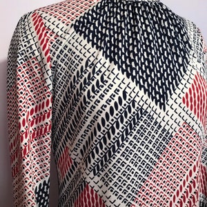 Op de afbeelding: Een wit, rood en blauw gebloemde blouse met lange mouwen en een geplooide halslijn.