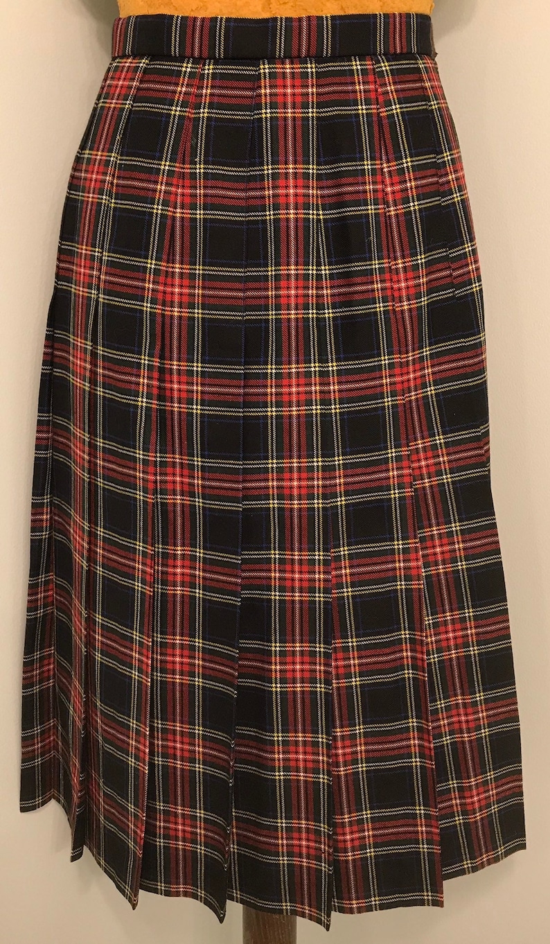 May include: A knee-length pleated skirt in a traditional tartan design. The pattern incorporates black, red, yellow, and blue checks. The skirt has a structured waistband and is made from a woven fabric, suitable for formal or casual wear.