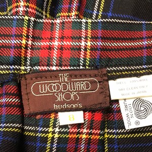 May include: Close-up of a vintage plaid skirt in red, green, yellow, blue, and white. The skirt has a label that reads "The Woodward Shops hudson's" and a size 8 tag. The fabric appears to be wool.