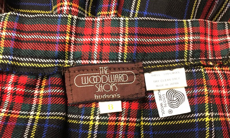 May include: Close-up of a vintage plaid skirt in red, green, yellow, blue, and white. The skirt has a label that reads "The Woodward Shops hudson's" and a size 8 tag. The fabric appears to be wool.