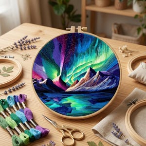 May include: A circular wooden embroidery hoop containing a needlepoint landscape of the aurora borealis over dark mountains and a reflective lake. The scene features vibrant threads in shades of blue, purple, green, and white.