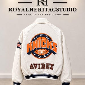 Può includere: Una giacca varsity color crema con un grande logo arancione e blu navy dei New York Knicks sul retro con il testo KITH all'interno. La parola AVIREX è ricamata sotto in blu navy. Una piccola toppa con la bandiera americana è sulla manica destra.