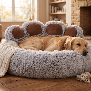 Può includere: Un cane dal pelo dorato chiaro riposa all'interno di una cuccia rotonda in peluche grigio chiaro. La cuccia presenta uno schienale alto a forma di zampa di animale con quattro cuscinetti marroni. Una coperta in maglia color crema è appoggiata.