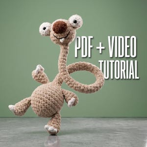 Puede incluir: Un animal de peluche tejido a ganchillo en color canela con un cuello largo, ojos grandes y redondos y una nariz marrón oscura. La criatura tiene un cuerpo redondo, cuatro extremidades con garras blancas y un cuello largo curvado. Texto PDF + VIDEO TUTORIAL.