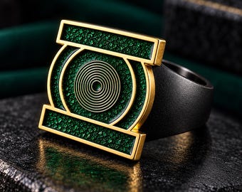 Op de afbeelding: Een ring met een goudkleurig rechthoekig frame en een centraal cirkelvormig embleem. Het embleem bevat een reeks concentrische cirkels omringd door een textuurrijke, donkergroene inleg. De ringband heeft een effen, matzwarte metalen afwerking.