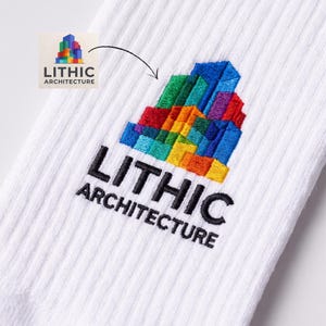 May include: A white ribbed sock featuring an embroidered logo of a multi-colored geometric building structure in shades of red, orange, yellow, green, and blue, with the black embroidered text LITHIC ARCHITECTURE positioned directly below it.