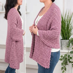 May include: A mauve, open-front crochet cardigan featuring a textured, chunky knit pattern with wide, three-quarter length sleeves. The garment is worn over a plain white top and blue denim jeans, showcasing a loose, relaxed fit and scalloped edges.