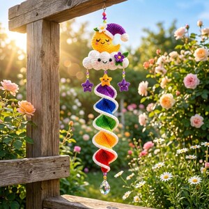 May include: A crochet hanging decoration featuring a yellow crescent moon with a purple nightcap, a white cloud with a smiling face, and a purple flower. Below, a rainbow-colored spiral tail hangs with small stars and a clear crystal prism.
