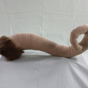 May include: A brown plush tail with a curled end. The tail is made of soft, fuzzy fabric and has a realistic look.